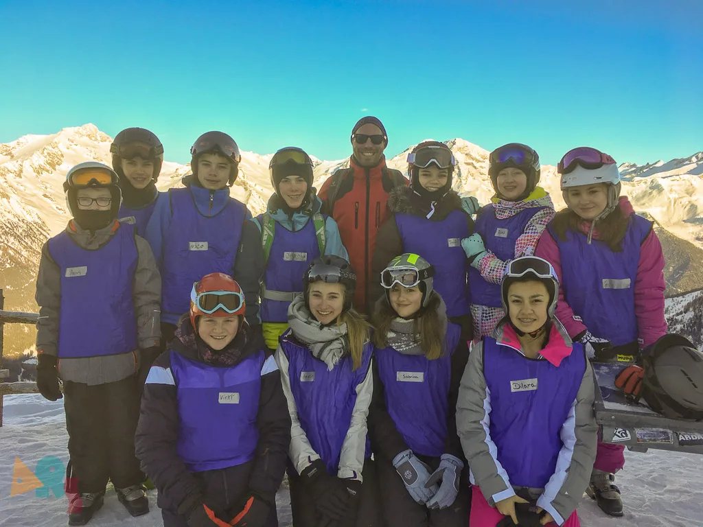 Skigruppe posiert vor der verschneiten Bergkette.
